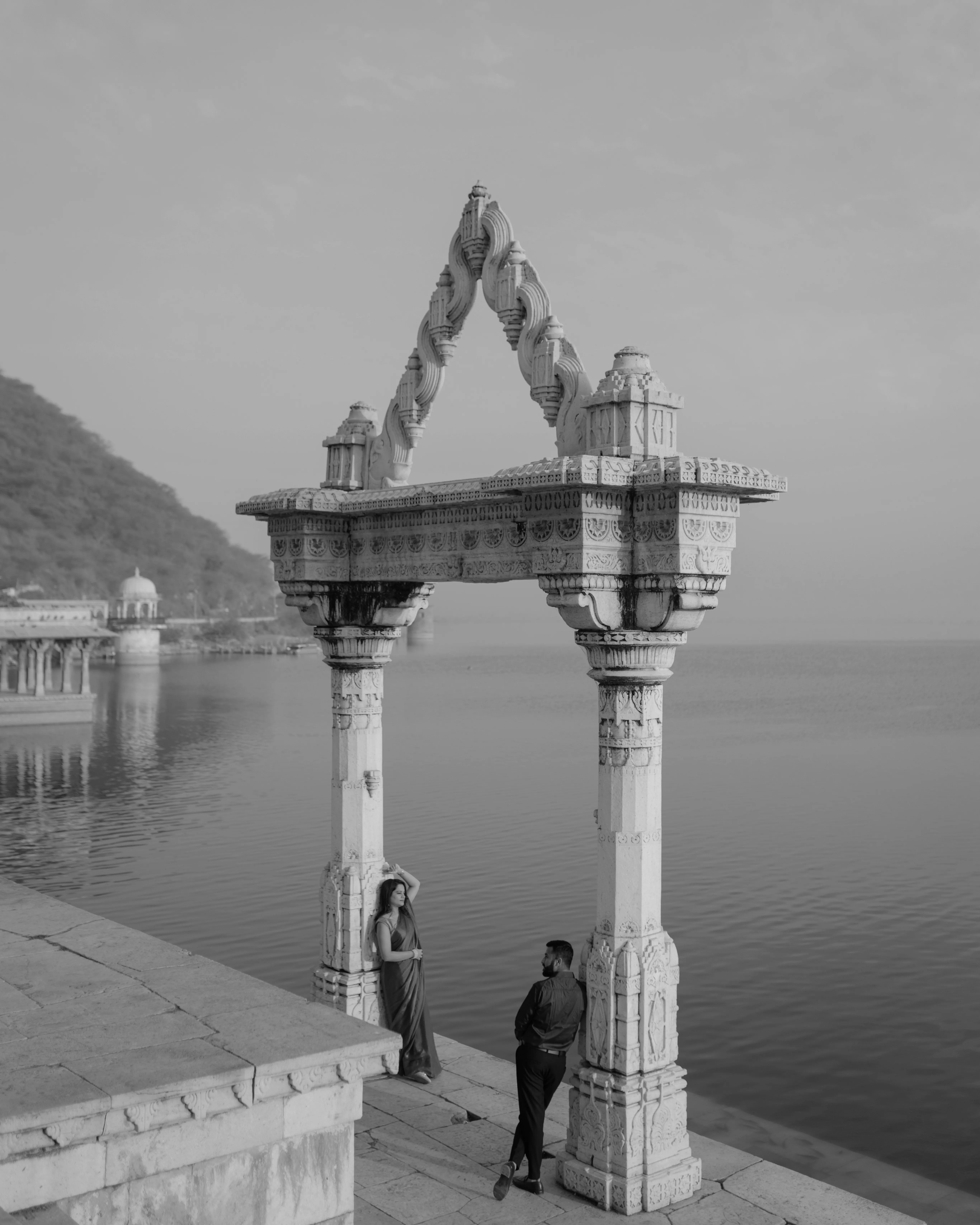 A couple sharing a quiet moment by the water beneath an ornate stone pavilion